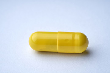 Closeup of one yellow pill on a white background with texture.