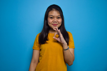 Portrait of Young beautiful asian women with blue isolated background, Smile and doing ok sign with fingers, excellent symbol
