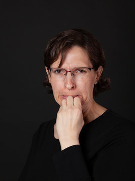 Woman in black with hand to mouth wearing glasses