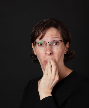 Woman in black with hand to mouth wearing glasses