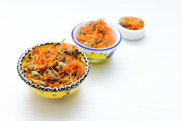 Petals of chopped dried calendula, displayed in containers on white wooden background