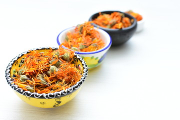 Petals of chopped dried calendula, displayed in containers on white wooden background