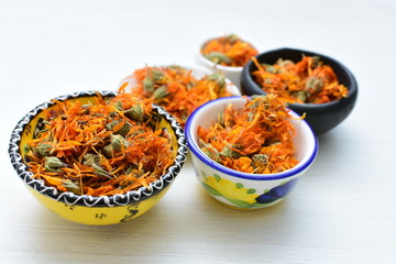 Petals of chopped dried calendula, displayed in containers on white wooden background