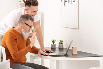 Young man teaching his father to handle with modern computer