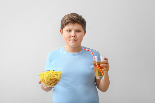 Overweight boy with chips and beverage on light background