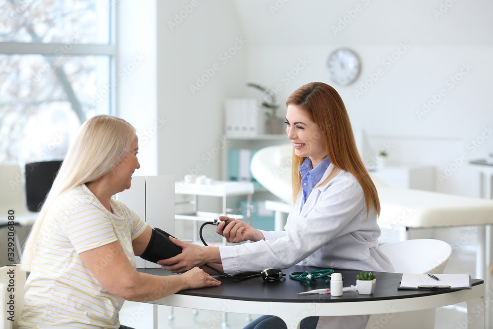 Poster Doctor measuring blood pressure of mature woman in clinic