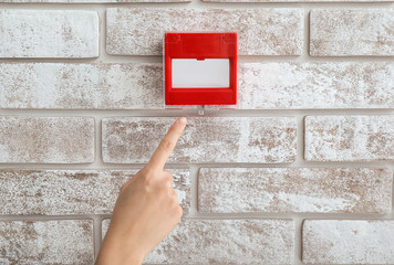 Hand of person near manual call point hanging on wall