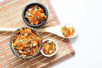 Petals of chopped dried calendula, displayed in containers on white wooden background