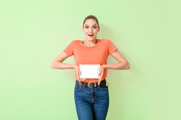 Naklejka premium Surprised young woman holding blank white digital tablet screen for copy space against green background, her expression conveys shock and amazement