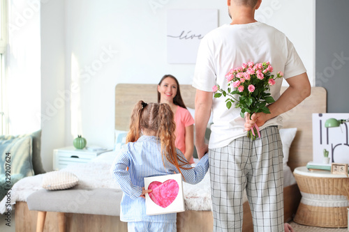 Husband and little daughter greeting woman to Mother's Day in bedroom