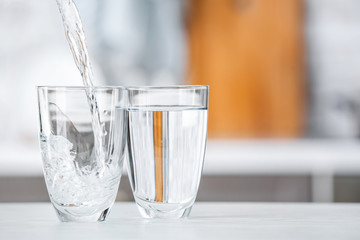 Pouring of fresh water into glass on table in kitchen