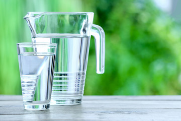 Glass and jug of fresh cold water on table outdoors