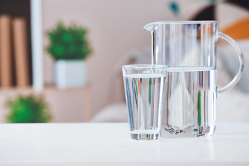 Glass and jug of fresh cold water on table in room