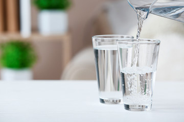 Pouring of fresh water into glass on table in room