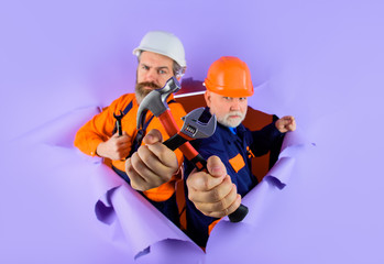 Through paper. Advertising. Worker in helmet. Repairman. Two repairman working with repair tools. Hammer. Spanner. Wrenches. Builder in construction helmet. Hard hat. Selective focus.
