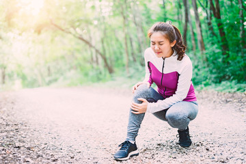 Fototapeta premium sport runner woman cramps in leg and feel pain, athletic young Asian girl in sportswear touching her knee ankle painful injury outside after exercise workout in nature road. Sports injuries concept