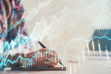 A woman hands writing information about stock market in notepad. Forex chart holograms in front. Concept of research. Double exposure