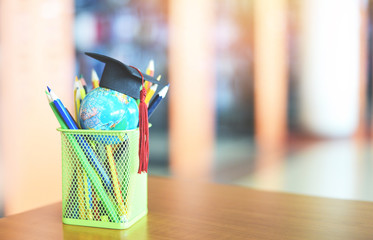 Education learning and back to school with graduation cap on a pencil case on the table in the library background - Graduation hat on earth globe model  global education study concept