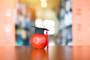 Education learning concept - Graduation cap on apple on the table with bookshelf in the library background
