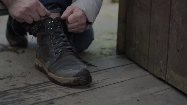 Hiker stops in rustic wooden building doorway to tie shoelaces on walking boots medium shot