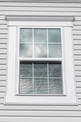Stand alone double hung window with fixed top sash and bottom sash that slides up, sash divided by two white grilles, surrounded by thick white elegant frame and decorative trim on a new residence
