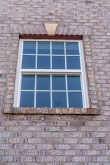 Fototapeta na wymiar Stand alone double hung window with fixed top sash and bottom sash that slides up, sash divided by three white grilles, surrounded by brick lintel and frame, decorative trim on a new residence