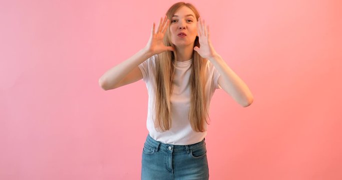 A young shocked woman in a white t-shirt , holding her hand near her mouth and telling a Secret, on a pink background, a girl screams