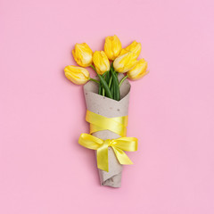 Blooming tulip flowers in craft paper package on pink background. Bouquet of yellow flowers as spring gift  for women or mothers day. View from above. Flat lay.