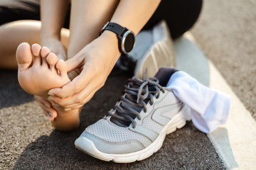 Running injury leg accident- sport woman runner hurting holding painful sprained ankle in pain. Female athlete with joint or muscle soreness and problem feeling ache in her lower body.