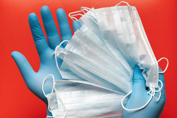 Doctor holds respiratory surgical face mask in hands blue medical gloves on red background. Pandemic corona virus, insurance, airborne diseases, SARS, grippe. Medical masks for human cover nose, mouth