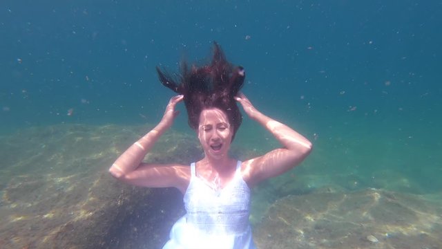 Young woman in a white dress lifting her arms to her head and screaming emotionally underwater