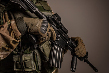 Detail of  soldier in military camouflage uniform protected with , body armour, holding machine gun...