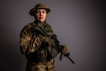 Obraz premium Portrait of soldier in military camouflage uniform protected with helmet, body armour, holding machine gun desaturated on a gray background.