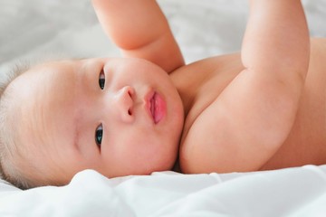 Portrait of a newborn Asian baby on the bed , Charming black-eyed baby 4 month old lies in bed,A child resting on a bed and looking