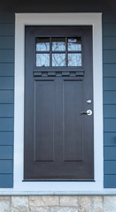 Hardwood black craftman front door on an entryway with dentil shelf and beveled glass, thich stiles and rails, white frame on a blue horizontal vinyl siding