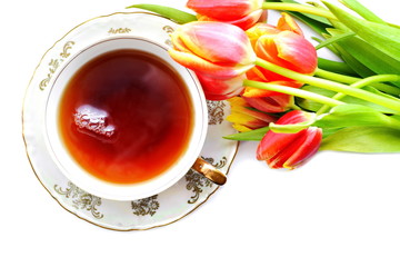 White porcelain pattern cup of hot black tea on dish with blurred Bouquet of flowers of red yellow blooming tulips with green leaf on isolated white background. Top view