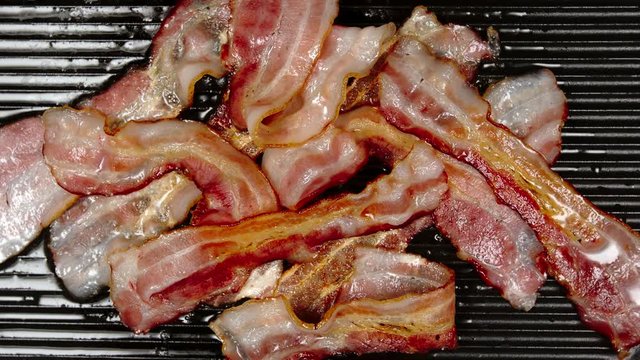 TOP VIEW: Heap of bacon are frying on a pan