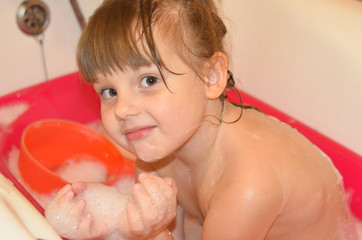Happy child takes a bath at home. Little girl doing water treatments for health
