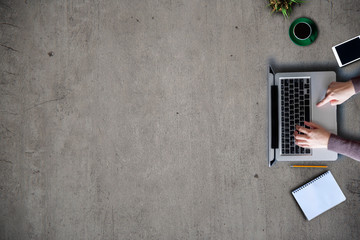 Female hands working on modern laptop. Office desktop on cement wall background.