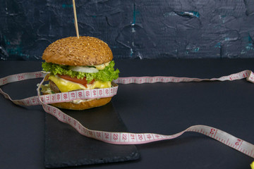 Hamburger for weight loss. The concept of losing weight. Juicy hamburger wrapped in measuring tape...