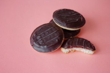A pile of Jaffa cakes. Bitten cookie covered with dark chocolate and filled with pink strawberry or cherry marmalade. Delicious biscuits isolated on pink background with copyspace