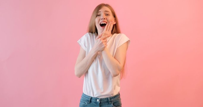 A young sad girl in a white t-shirt is experiencing a toothache, on a pink background
