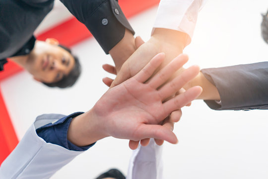 Bottom view of asian professional workers putting hands together piling on top of one another, businessmen, doctors, architectures, engineer and colleagues, standing around each other in a circle.