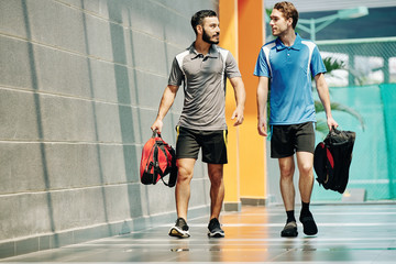 Sportsmen discussing news when walking in corridor of health club with gym bags