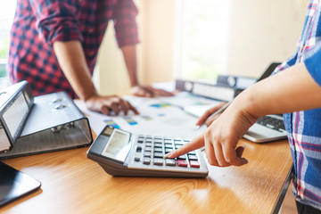 businesswoman and businessman working together as a group in an office, using a pen and calculator, explaining and planning strategy analyzing and calculating data and statistics of charts and graphs