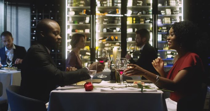African American young handsome man and beautiful woman having dinner in restaurant. Couple eating desert and drinking wine. Boyfriend and girlfriend talking cheerfully on romantic first date concept.