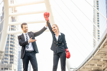 Business coworkers fighting each with wearing boxing gloves and the referee announcing the winner, representing anger, problems, issues or stress within the work environment, in urban city district
