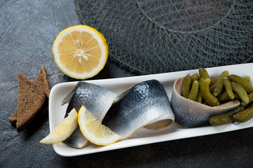 Closeup of a plate with herring fillet, pickles, brown bread and lemon, studio shot on a brown...