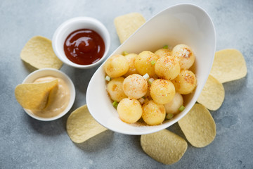 Bowl of roasted potato balls, potato chips and dips over light-blue stone background, elevated view