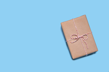 A layout of a brown wrapping present with white and red string bow laying on a blue background, representing elegances copy space of gifts for Christmas, valentine’s day, birthday and special events